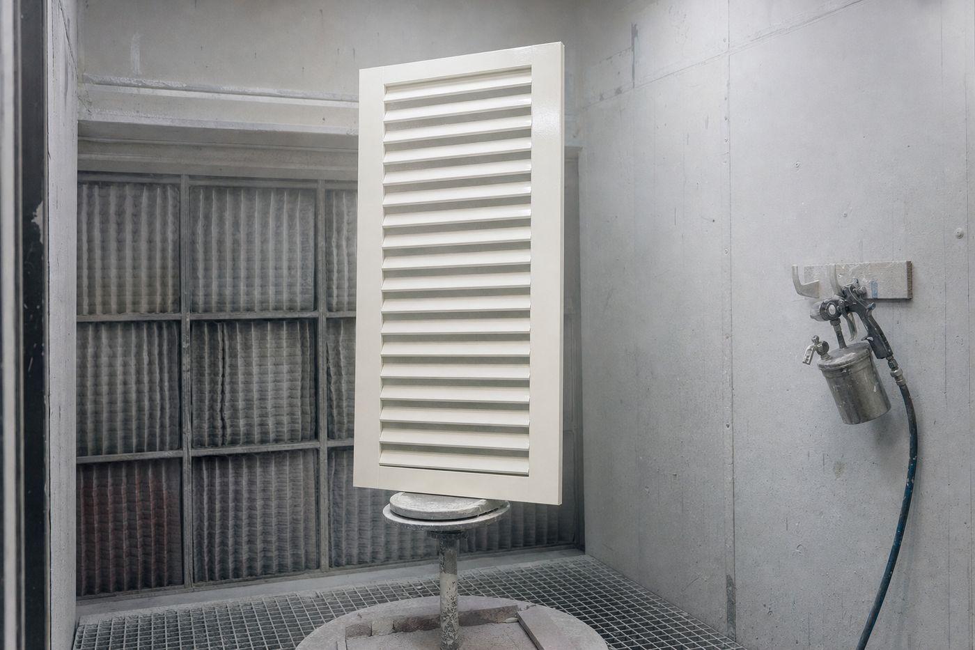 Volet bois persienné dressé sur tourniquet dans une cabine de peinture, lames recouvertes d’une finition fraîchement appliquée au pistolet