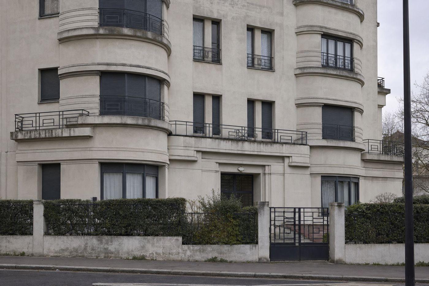 Immeuble Art déco des années 1920-1930 en centre urbain dense, façade en enduit clair aux angles arrondis, garde-corps en ferronnerie géométrique et volets métalliques gris à lames étroites