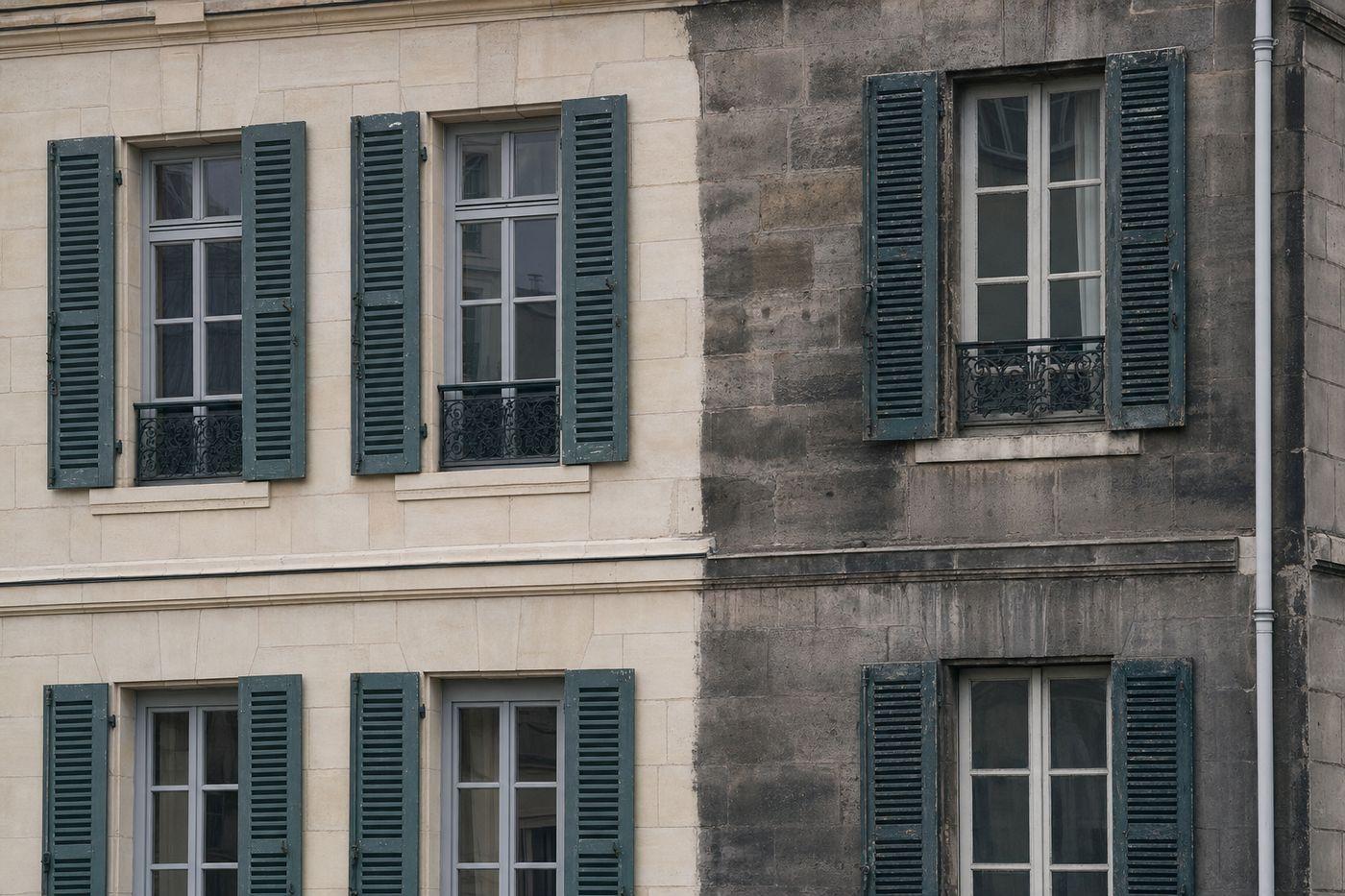Façade parisienne en pierre de taille à mi-nettoyage : la moitié gauche ravalée en crème clair, la moitié droite encore grise de suie, avec les mêmes volets fatigués des deux côtés
