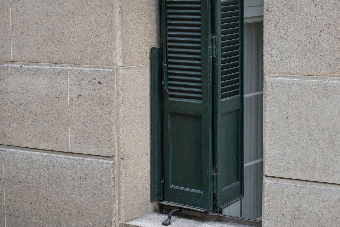 Volet parisien à demi replié dans l’épaisseur de l’embrasure en pierre : vantail extérieur rabattu contre le jambage, vantail intérieur encore ouvert, penture centrale visible