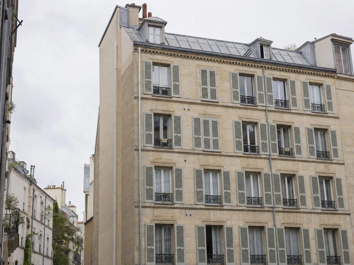 Immeuble parisien du quartier des Batignolles dans le 17e arrondissement, façade en pierre de taille sobre, garde-corps simples et persiennes métalliques gris-vert