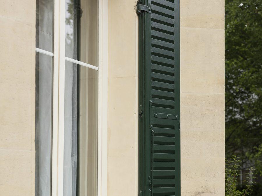 Persienne métallique parisienne repliée dans l'embrasure d'une fenêtre, lames horizontales et pentures apparentes