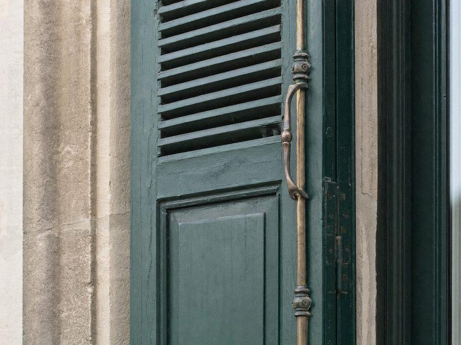 Volet parisien replié dans l'embrasure d'une fenêtre en pierre de taille, partie haute persiennée et panneau plein en bas, peint en vert foncé, espagnolette en laiton